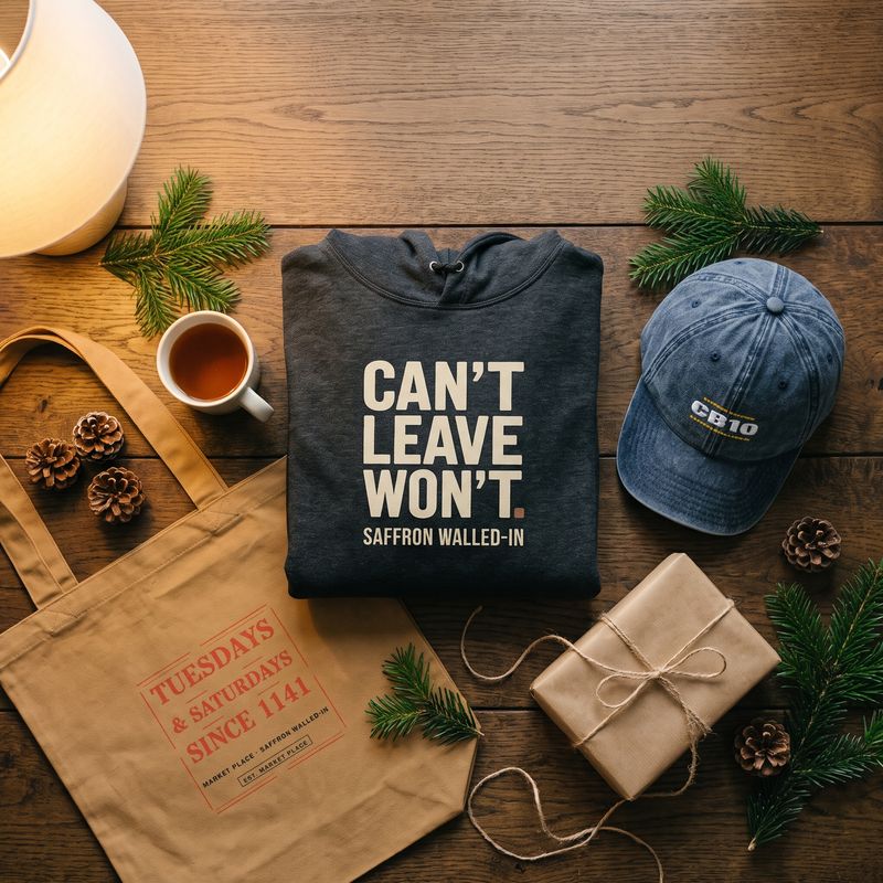 Christmas gift flat-lay: the folded CAN'T LEAVE. WON'T. hoodie and a CB10 cap with pine sprigs, a wrapped parcel and a mug of tea on an oak table